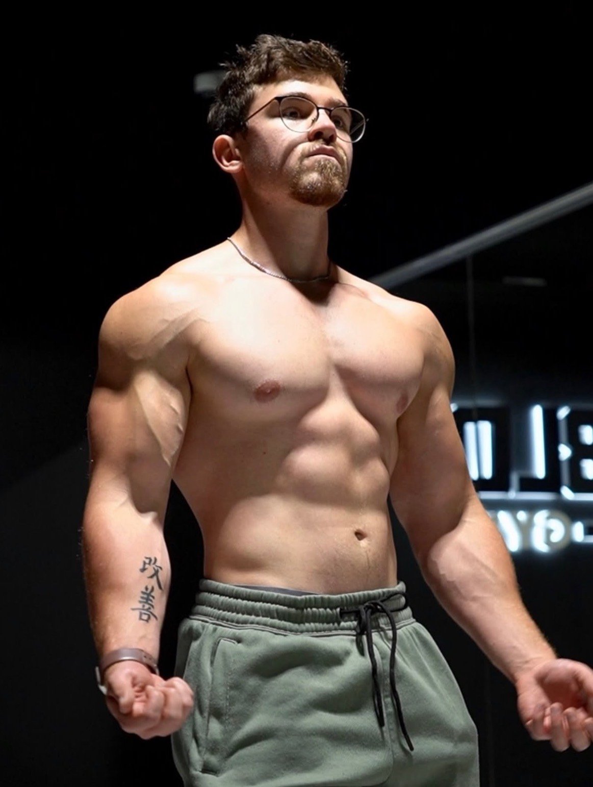 Lance Parker, founder of Broken Limits Training, stands shirtless against a dark background in olive shorts, arms at his sides